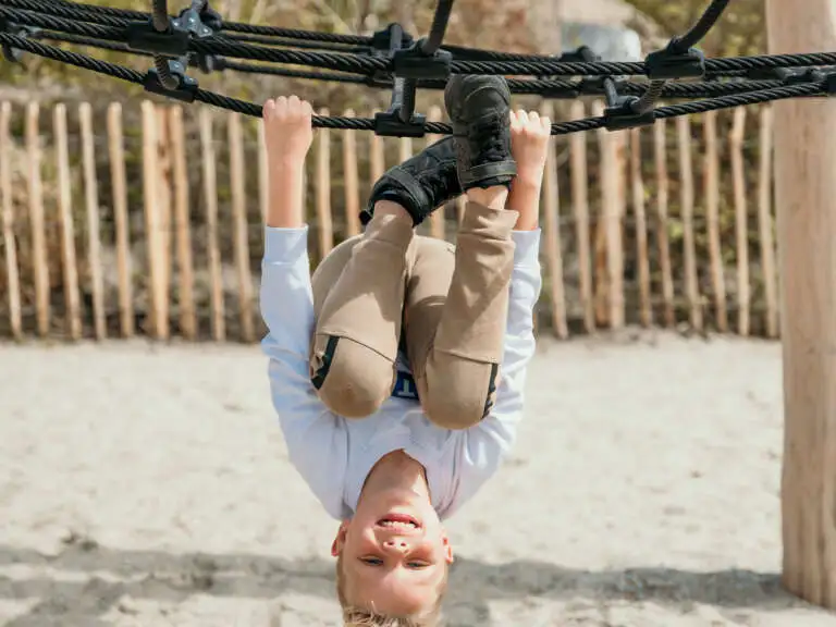 Jongen klimt en speelt in de nieuwe houten buitenspeeltuin dichtbij het strand