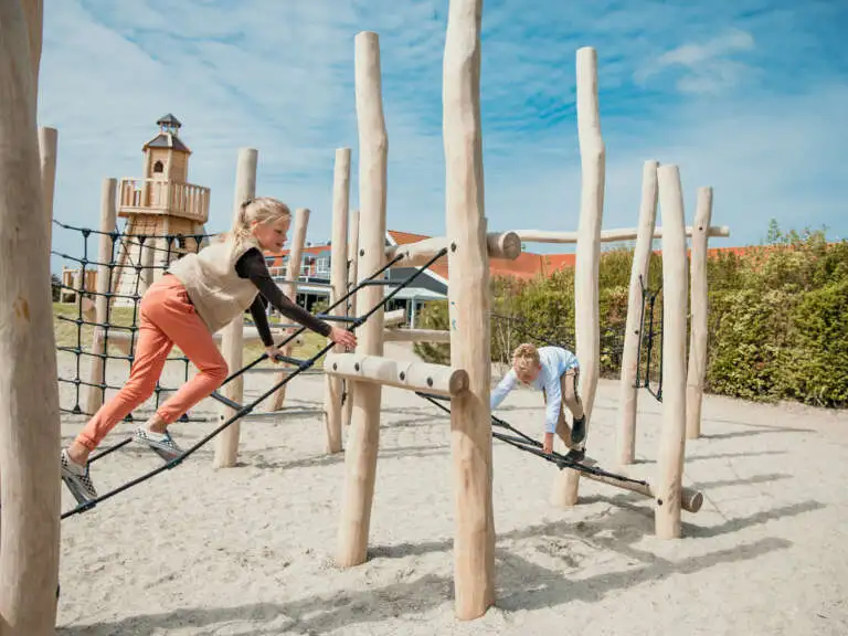 Grote zus klimt op het nieuwe klimrek samen met kleine broer dichtbij het strand