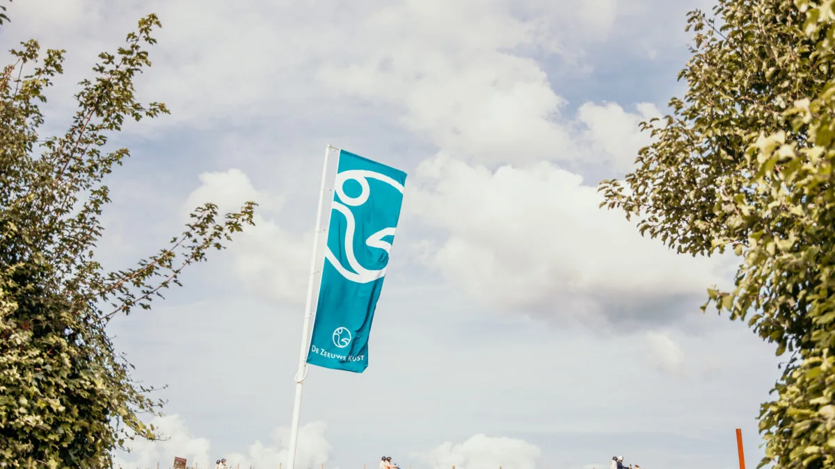 Blauwe milieuvriendelijke vlag wappert op Strandpark De Zeeuwse Kust met groene bomen en een dijk op de achtergrond