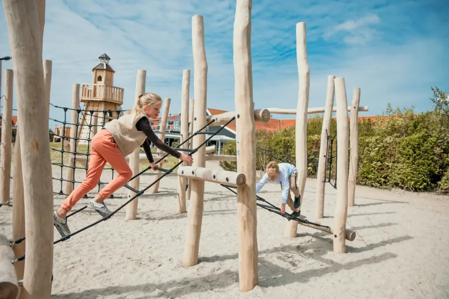 Grote zus klimt op het nieuwe klimrek samen met kleine broer dichtbij het strand