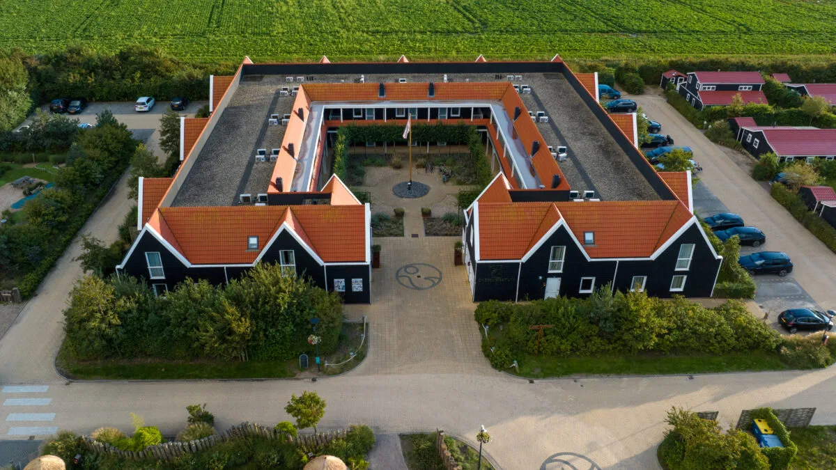 Luchtfoto van het hoofdgebouw op Strandpark De Zeeuwse Kust met karakteristieke Zeeuwse architectuur een groene omgeving en ruime parkeerplaatsen