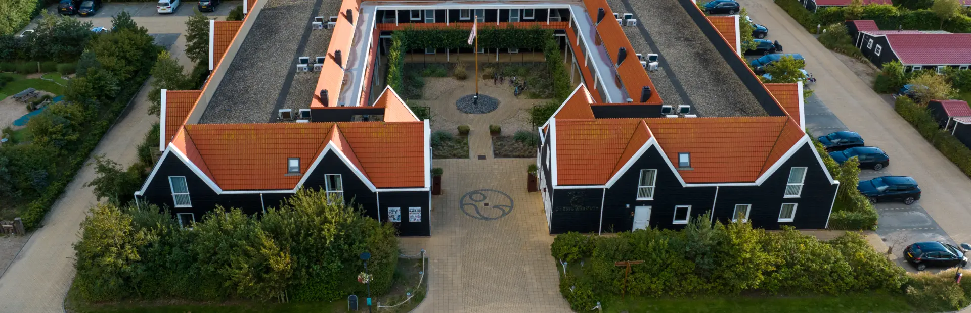 Luchtfoto van het hoofdgebouw op Strandpark De Zeeuwse Kust met karakteristieke Zeeuwse architectuur een groene omgeving en ruime parkeerplaatsen